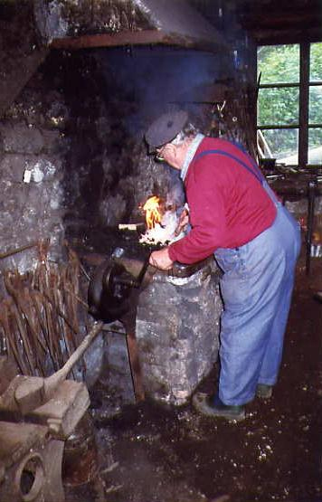 Photographie d'un des derniers forgerons du Dauphiné, s'affairant au dessus de sa forge pour forger un outil