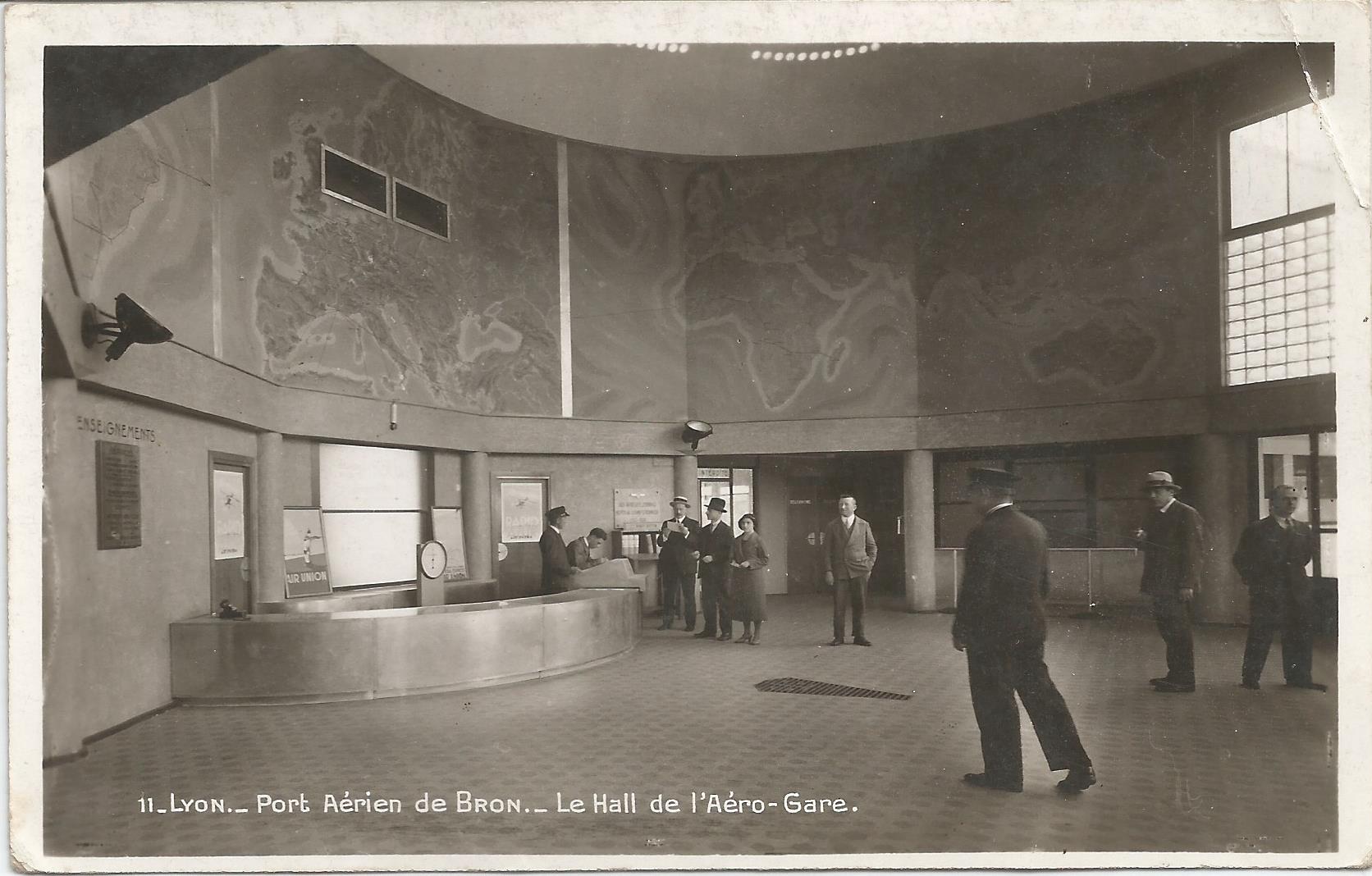 Photographie présentant le grand hall de l'aérogare, conçu par les architectes Chomel et Verrier, vers 1932. Des peintures représentant les continents sont présentes sur les murs en hauteur.
