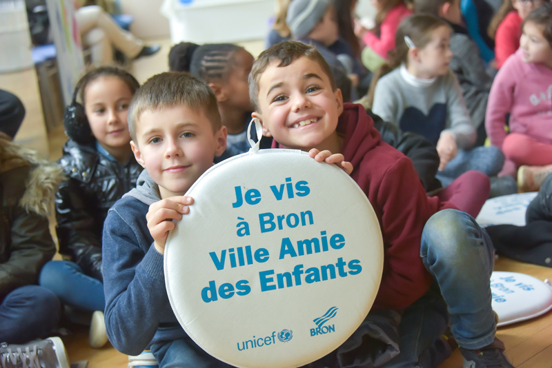 Deux enfants tenant un coussin avec le label "Ville amie des enfants"