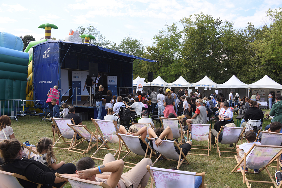 Pendnat la Fête des animaux 2024, une scène est installée sur la Prairie du Fort de Bron, avec des chaises longues pliantes et des chaises devant. un concours du plus beau chien se déroule devant les habitants assis. Les tentes des exposants sont visibles dans le fond de la photo, devant les arbres du parc du Fort de Bron..