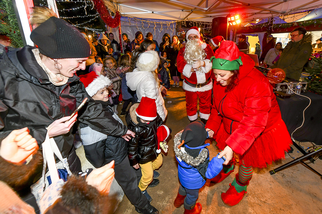 Des personnes déguisées en lutins et le Père Noël dansent avec des enfant et leurs parents sous la tente de la Boum du Père Noël pendant le marché de Noël 2024.