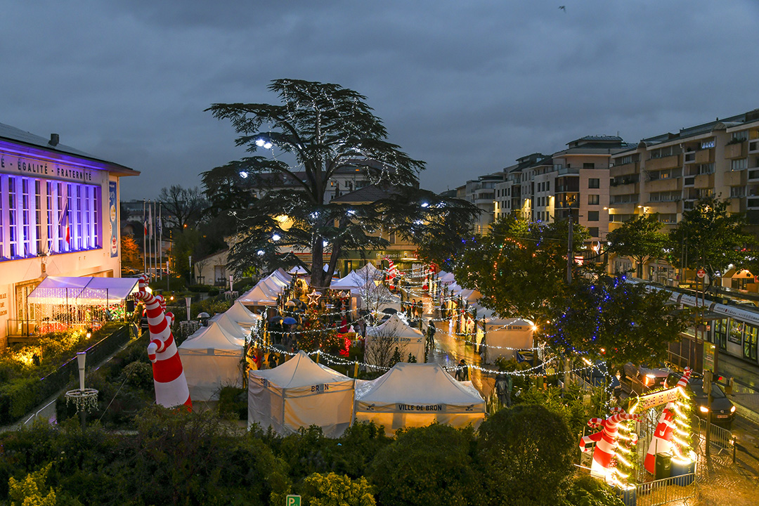 vue aérienne du marché de Noël de Bron à la tombée de la nuit, sur la place de Weingarten, devant l'Hôtel de Ville. Des décorations, sapins et illuminations éclairent la place et les habitants circulent entre les tentes des marchands.