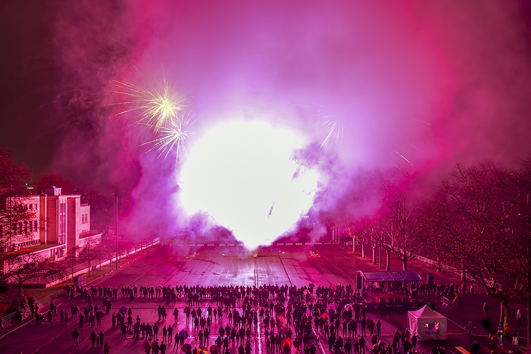 Explosion de lumière sur la place de la liberté pendant le feu d'artifice du 8 décembre 2024. La foule rassemblée observe le feu d'artifice sur le parking avec beaucoup de fumée dans l'atmosphère.