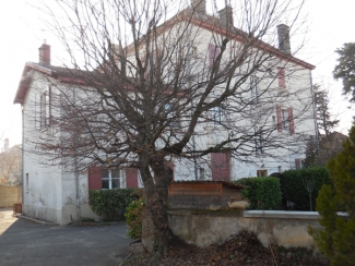 La Maison Forte de Bron, un bâtiment ancien en deux parties, un grand donjon cubique avec un toit pyramidal sur la droite et une dépendance plus petite cubique accolé à sa gauche, avec un toit à double pente. Des cheminées percent les toits et un petit muret se tient devant, avec un arbre sans feuilles. 