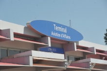 Vue partielle du bâtiment du Terminal de l'aéroport d'affaires de Lyon-Bron. Architecture en béton clair avec des rangées de fenêtres, des paresoleils rouges et un grand panneau ovale bleu affichant "Terminal Aviation d'Affaires".