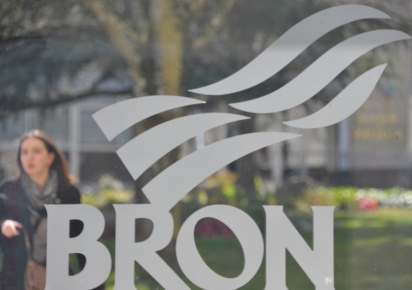 Logo de la Ville de Bron sur une vitrine, avec le square Grimma et fond. Une jeune femme passe dans en arrière plan.