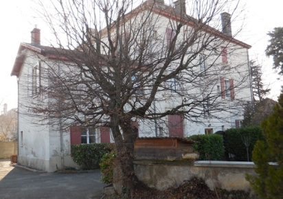 La Maison Forte de Bron, un bâtiment ancien en deux parties, un grand donjon cubique avec un toit pyramidal sur la droite et une dépendance plus petite cubique accolé à sa gauche, avec un toit à double pente. Des cheminées percent les toits et un petit muret se tient devant, avec un arbre sans feuilles. 