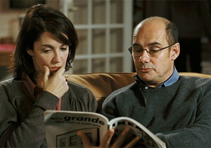 Zabou et Bernard Campan assis sur un canapé en train de feuilleter un catalogue d'ameublement.