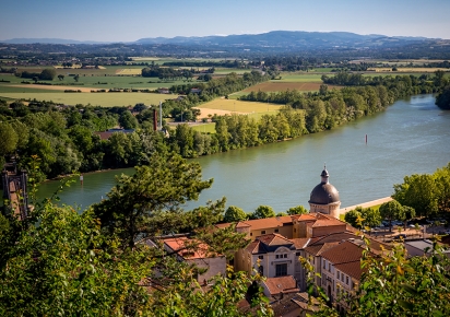 Photographie en couleur, vu de hauteur, sur la Saône, avec la campagne en fond et un village arboré au premier plan.