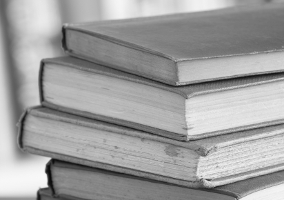 Photographie en noir et blanc représentant un empilement de livres anciens. Le fond de l'image est flou, quelques livres sont tâchés.