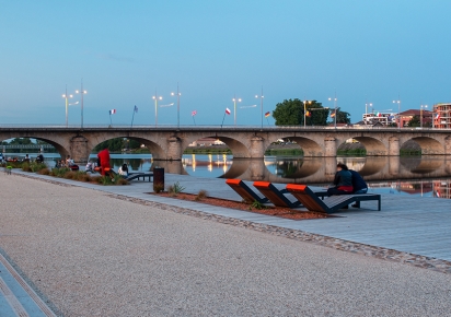 Vue du Pont de Roanne depuis les quais en début de soirée, avec des terasses en bois et des chaises longues au premier plan